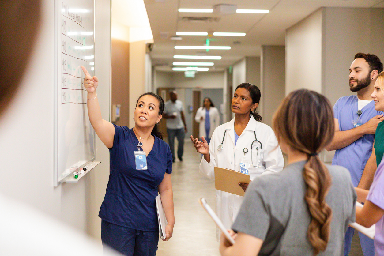 A Nurse Leader Points to a White Board and Speaks to a Medical Team