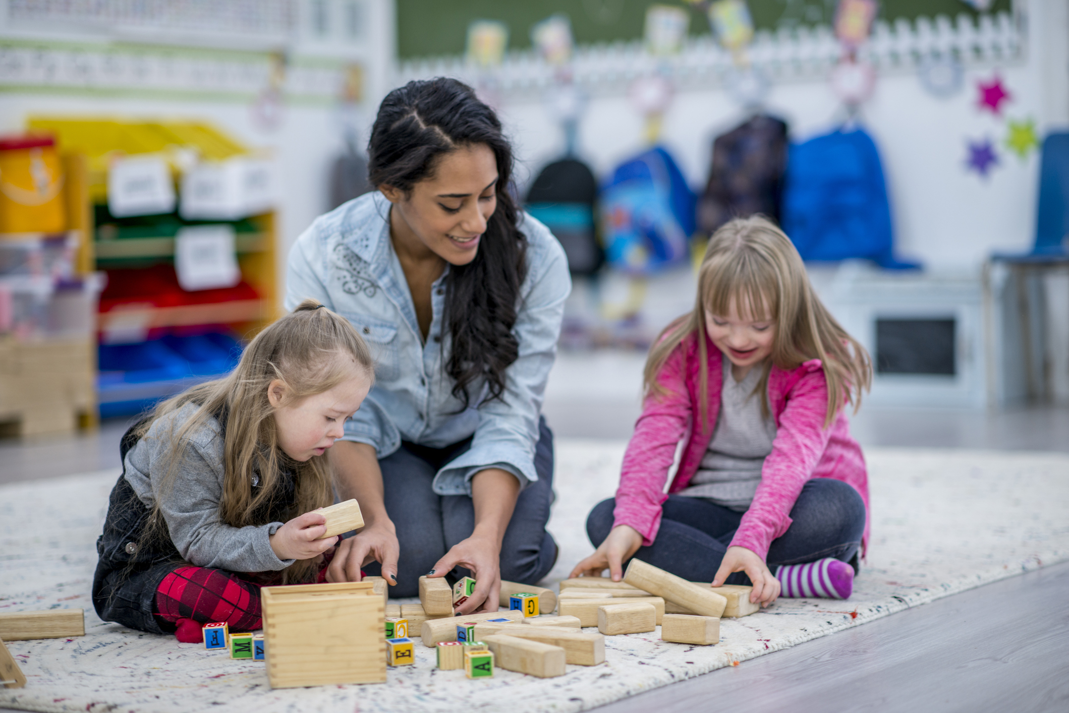 A special education teacher plays with two students on the floor in a classroom.