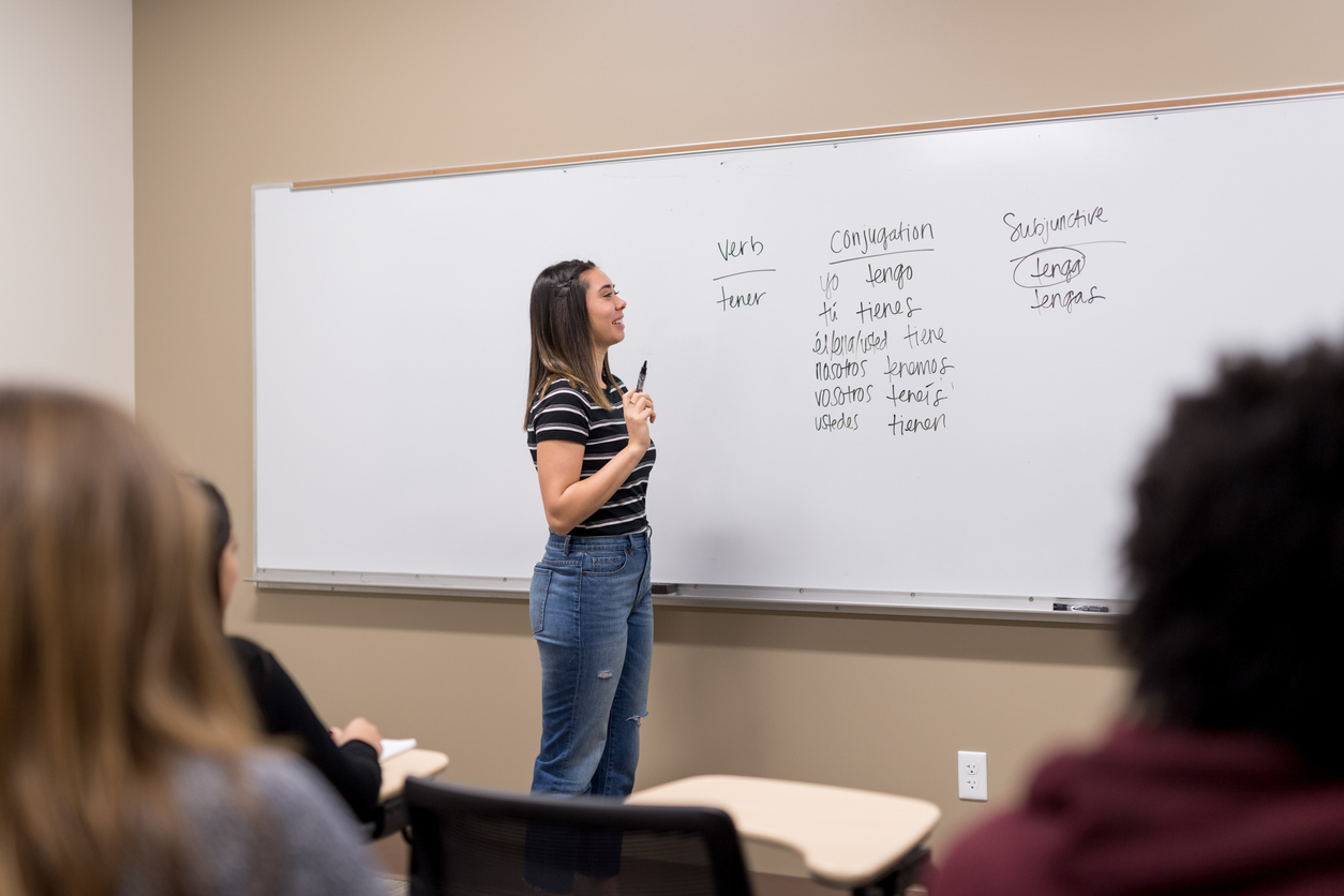 An ESL teacher stands at the front of a classroom and points to words on a whiteboard