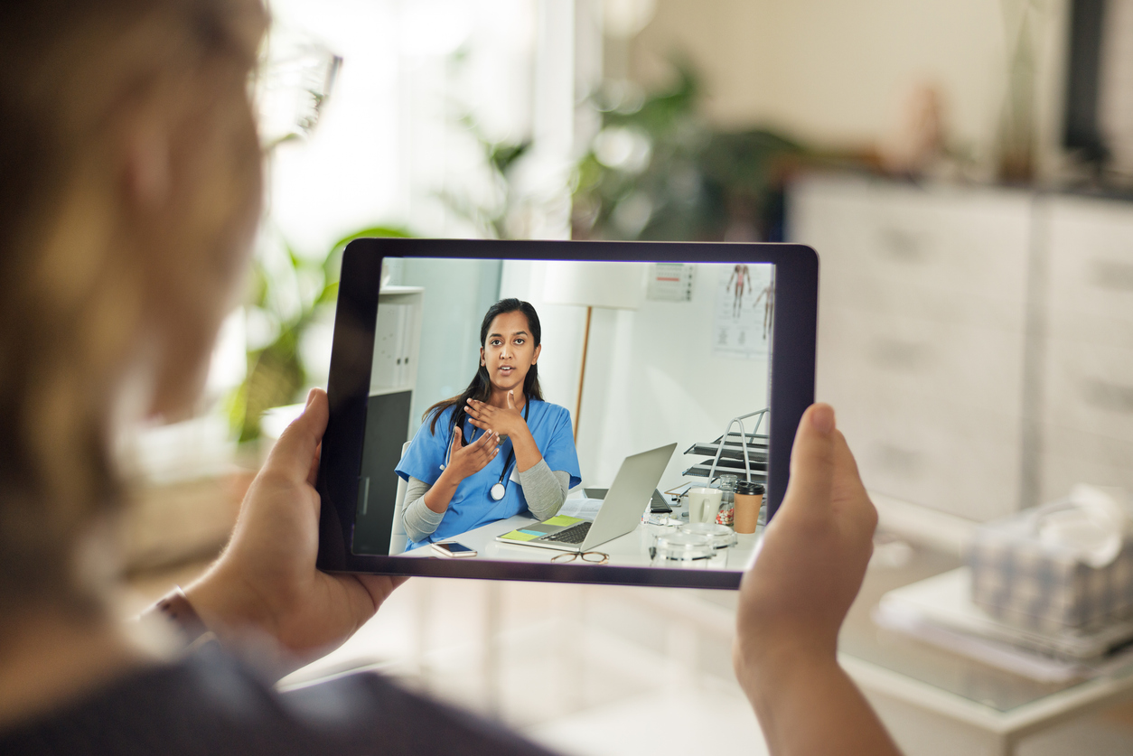A patient holds a tablet showing a nurse conducting a telehealth appointment